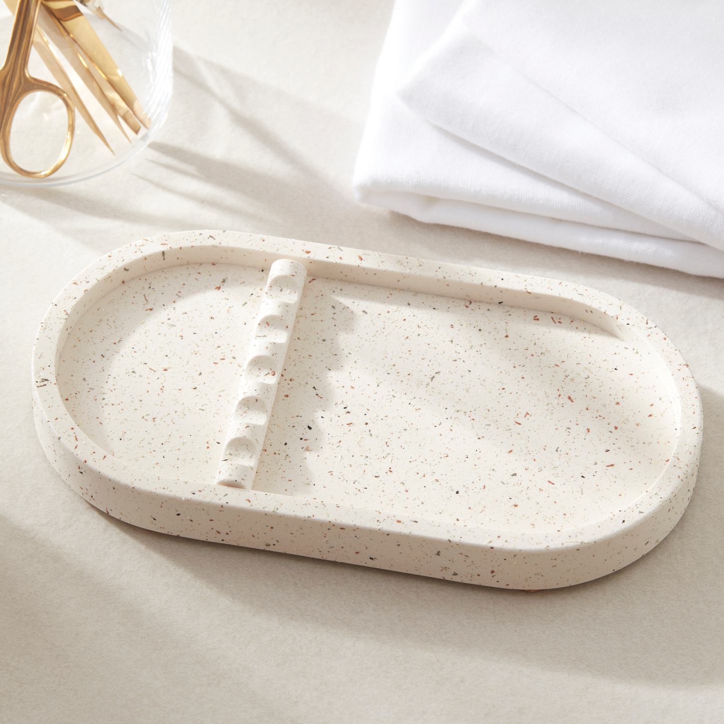Speckled beige ceramic tray on a light surface with white cloth and gold scissors in the background.